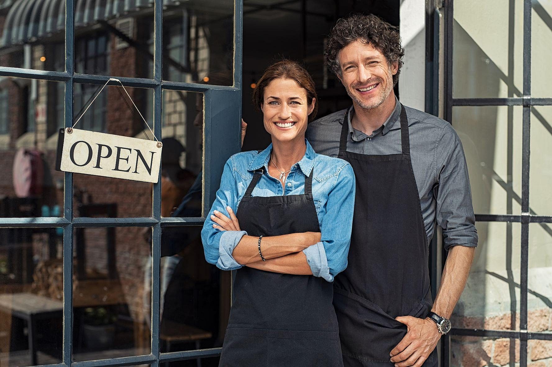 Woman and man business owners standing in front of their shop